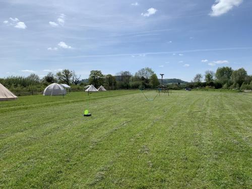 a field with tents and a green object in the grass at Stunning 5-Bed Cabin in Ashton Under Hill in Evesham