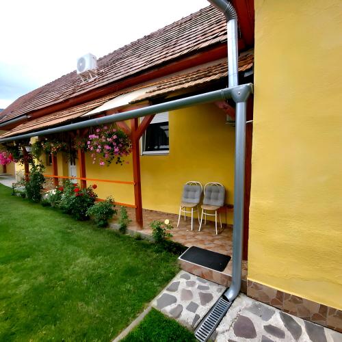 a yellow house with two chairs sitting under a roof at Kata Vendégház in Sátoraljaújhely