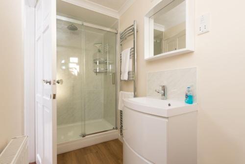 uma casa de banho branca com um lavatório e um chuveiro em Talland Croft em Crantock