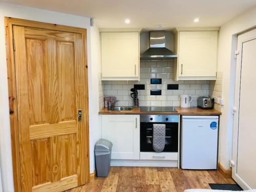 Mc Courts Barn, Tiny house in the Mournes في Hilltown: مطبخ بدولاب بيضاء وباب خشبي