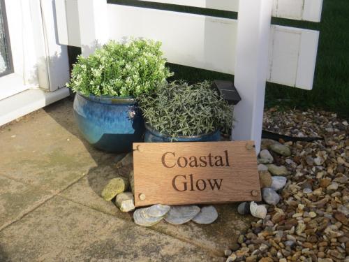 a wooden sign that reads coastal glow next to two potted plants at Coastal Glow in Heacham