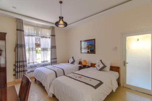 two beds in a room with white walls and windows at The Moon River Homestay & Villa in Hoi An