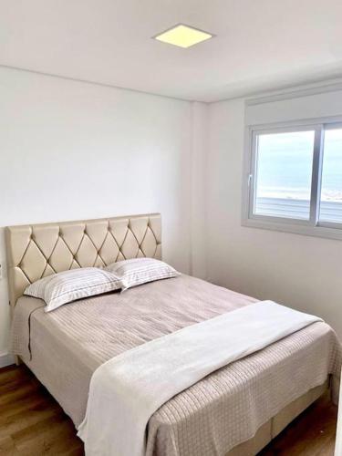 een witte slaapkamer met een bed en een raam bij Apto em Navegantes/Gravatá in Navegantes