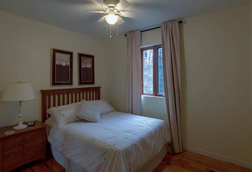a bedroom with a bed with a ceiling fan and a window at Chalet des bouleaux in Nominingue
