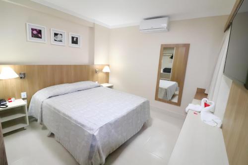 a white bedroom with a bed and a mirror at PIAZZA DIROMA ACESSO A PARKS in Caldas Novas