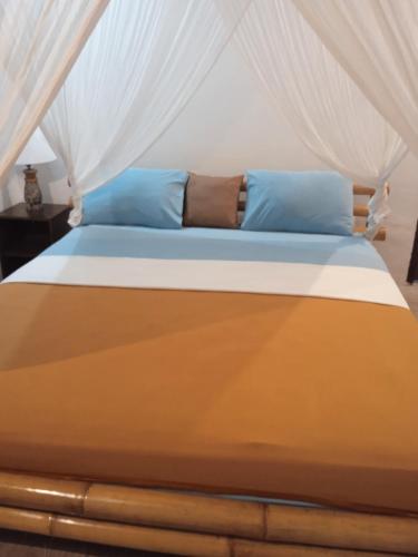 a bed with white curtains and blue pillows on it at Gili Air Santay 3 in Gili Air