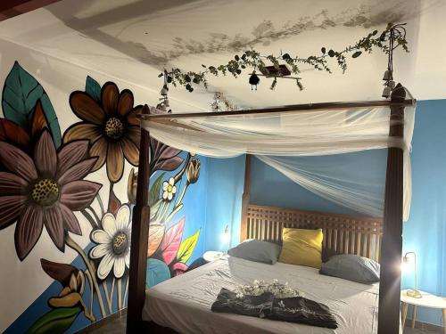 een slaapkamer met een hemelbed en een muurschildering van bloemen bij Maison de 3 chambres avec piscine privee terrasse et wifi a Sainte Anne a 9 km de la plage in Sainte-Anne