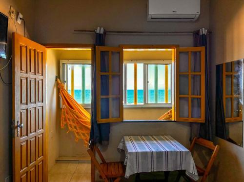 Cette chambre dispose de deux fenêtres, d'une table et d'une porte. dans l'établissement Kitnet beira mar com WiFi em Arembepe Camacari BA, à Camaçari