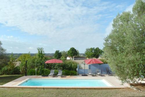 een zwembad met 2 parasols en stoelen bij Maison à 6 km de Eymet piscine chauffée. in Roumagne