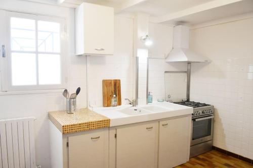 a white kitchen with a sink and a stove at Maison à 6 km de Eymet piscine chauffée. in Roumagne