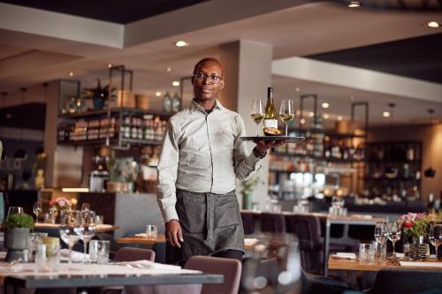 a man holding a tray of wine glasses in a restaurant at Van der Valk Hotel Stein Urmond in Urmond