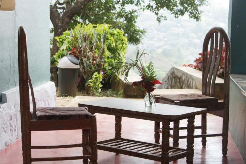 dwa krzesła i stół na balkonie ze stołem i krzesłami w obiekcie Madhuvana Guest House w mieście Madikeri