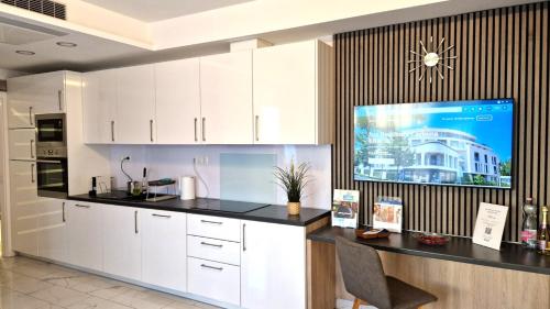 a kitchen with white cabinets and a tv on the wall at Spa Residence Carbona 101, 307 Apartman in Hévíz