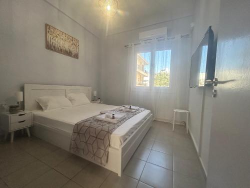 a white bedroom with a bed and a window at AKTIS apartment 3 near airport in Artemida