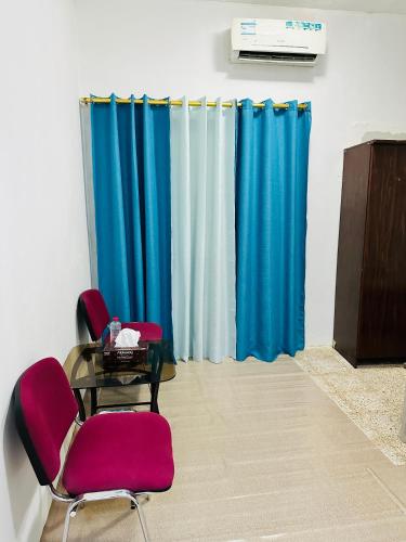 Habitación con 2 sillas, mesa y cortinas azules en Room for rent, en Sharjah