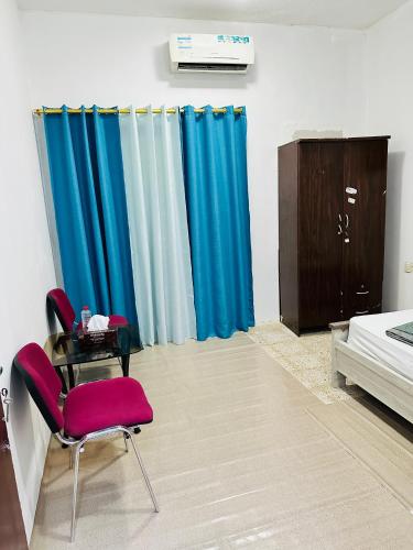 1 dormitorio con cortinas azules, mesa y cama en Room for rent, en Sharjah