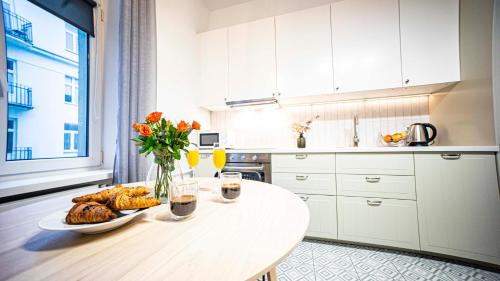 a white kitchen with a table with bread and flowers at Spacious Apartment with 3 meter ceilings, Powiśle, The Old Town in Warsaw