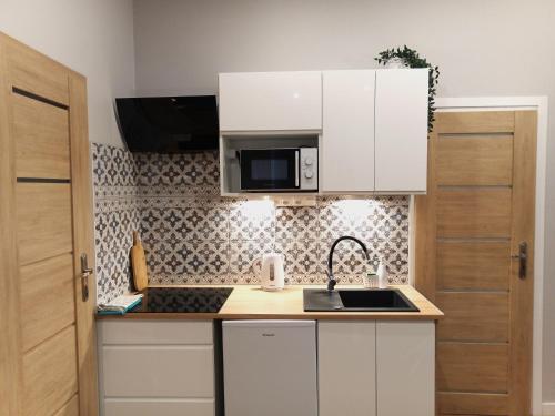 a kitchen with white cabinets and a sink and a microwave at Apartament na Przedmieściu in Wrocław
