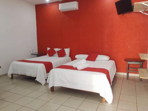 two beds in a room with a red wall at Hotel y Bungalows Bugambilias in San Patricio Melaque