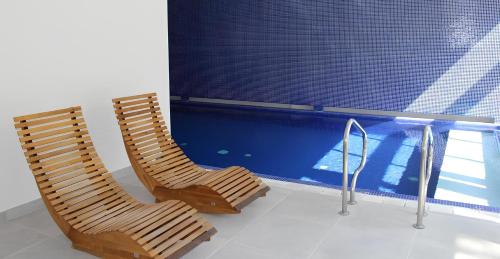 2 sedie in legno sedute accanto alla piscina di Les Pleiades Hôtel-Spa-Restaurant a Barbizon