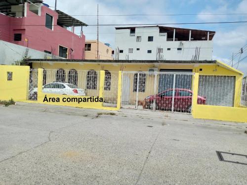 une clôture jaune avec deux voitures garées derrière elle dans l'établissement Acuarela del Rio H#3 Cerca Aeropuerto y Terminal Habitación privada con baño, à Guayaquil
