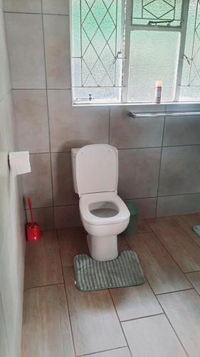 a bathroom with a toilet with a window and a rug at Secret Guest House in Pietermaritzburg