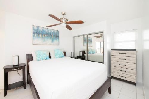 a white bedroom with a bed and a ceiling fan at Cayman Reef Resort #52 in George Town