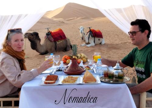 a man and a woman sitting at a table in the desert at Nomadica Luxury Camp in Merzouga