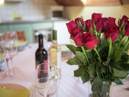 a vase of red roses sitting on a table with wine glasses at Spacious atmospheric upper floor of a farmhouse with garden in Wuustwezel