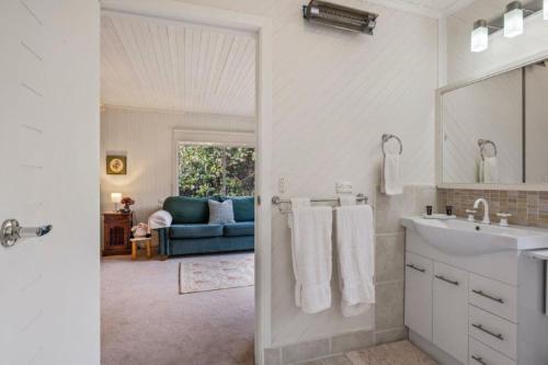 a white bathroom with a sink and a blue couch at Roses on the River - An absolute river frontage cottage in Bright