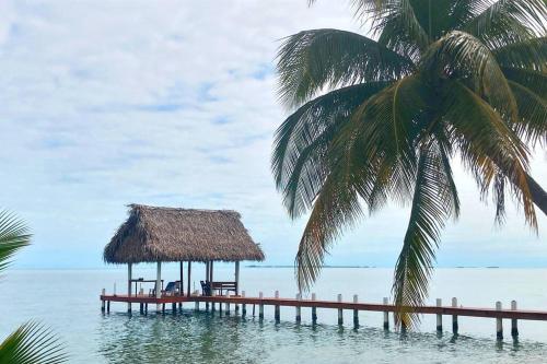 a pier with a hut in the water with a palm tree at The Tiki Toucan Tropical Suite + Private Pool in Placencia Village