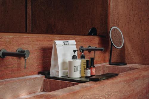 a bathroom counter with a sink with a mirror and cosmetics at Further Hotel in Canggu