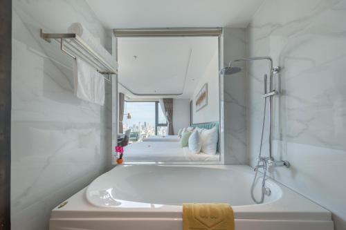 un bagno bianco con vasca e specchio di Cordial Hotel and Spa a Da Nang