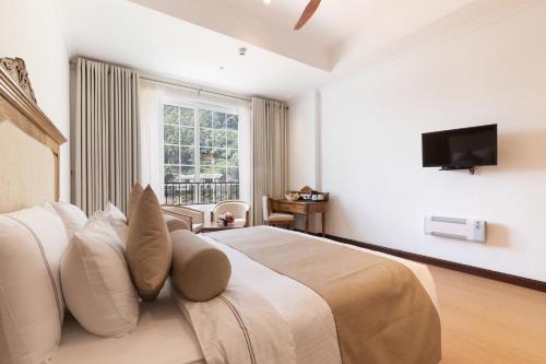 a bedroom with a bed with white pillows and a television at Araliya Red - Budget friendly Hotel- Where you find stunning 360 panoramic view of Nuwara Eliya in Nuwara Eliya