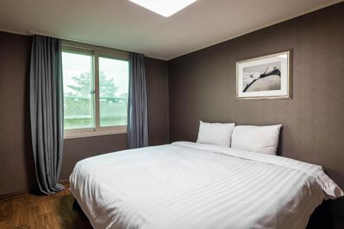 Un dormitorio con una gran cama blanca y una ventana en Kensington Resort Jeju Hanlim, en Jeju