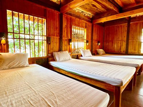 two beds in a room with wooden walls and windows at Dao Homestay in Hoàng Su Phì