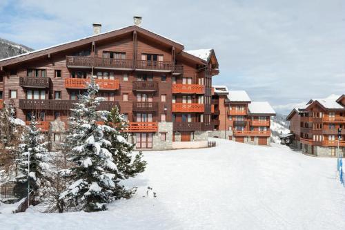 un grand bâtiment dans la neige avec un sapin de Noël dans l'établissement Quartier La Forêt - maeva Home - Studio 3 Personnes - Budget MAE-3627, à Valmorel