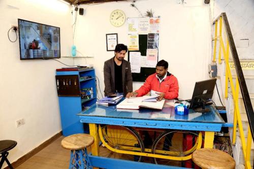 deux hommes assis à une table avec un ordinateur portable dans l'établissement Bunk Hostel Delhi Best Backpacking Accommodation, à New Delhi