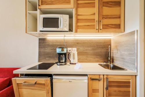 une petite cuisine avec un évier et un micro-ondes dans l'établissement Résidence Le Hameau du Sauget - maeva Home - 2 Pièces 4 Personnes Sélection MAE-3483, à La Plagne Tarentaise