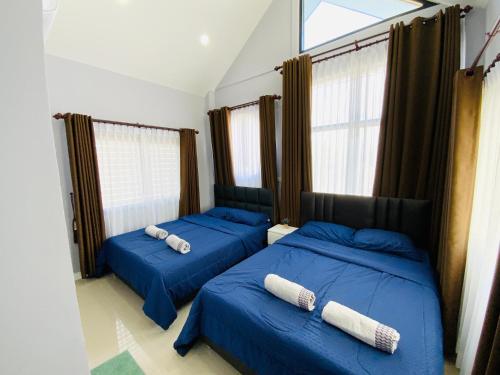 2 Betten mit blauer Bettwäsche in einem Zimmer mit Fenstern in der Unterkunft Patteera Pool Villa Sattahip in Sattahip
