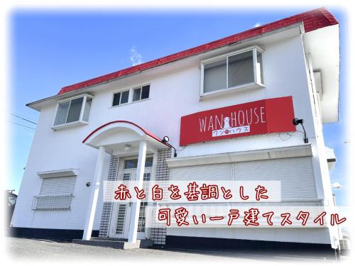 een wit gebouw met een bord voor een knipoog huis bij ワンハウスatワニベース in Otsu