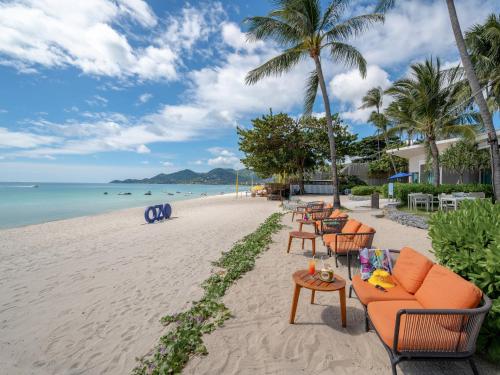 una spiaggia con sedie e tavoli e l'oceano di OZO Chaweng Samui a Chaweng Beach