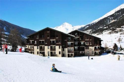a child sitting in the snow in front of a ski lodge at Studio 4 pers pied des pistes 80267 in Lanslevillard