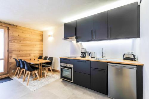 une cuisine avec des armoires noires et une table avec des chaises dans l'établissement Quartier Crève Cœur - maeva Home - Appartement 2 pièces 6 personnes skis aux pieds - Prestige - Super Home MAE-0476, à Valmorel