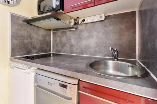 uma cozinha com um lavatório de aço inoxidável e armários vermelhos em Studio accès direct aux pistes à la Mongie 84848 em La Mongie