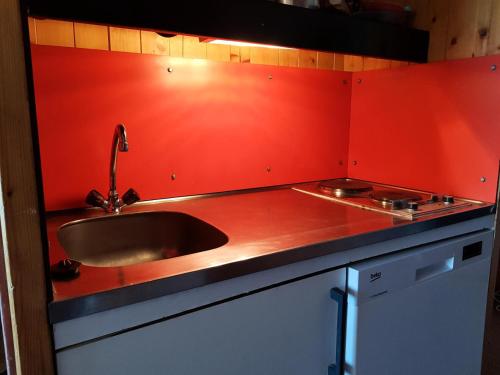 - une cuisine avec un évier et un mur rouge dans l'établissement Résidence Adret - Studio pour 4 Personnes 76, à Arc 1600
