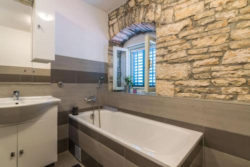 a bathroom with a tub and a sink and a stone wall at Villa La Musica by Istrialux in Čabrunići