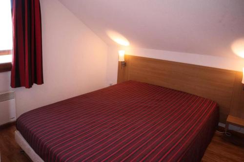 um quarto com uma cama com um cobertor listrado vermelho em Résidence LES CHALTES BOIS MEAN - 2 Pièces pour 4 Personnes 074 em Les Orres
