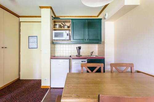 une cuisine avec des placards verts et une table en bois dans l'établissement Résidence L'Alpaga - maeva Home - Appartement 2 Pièces 5 Personnes - Budget MAE-2484, à La Salle Les Alpes