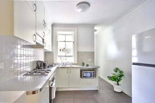 a white kitchen with a sink and a microwave at Elegant 2 BR on the edge of Downtown Dowling St 2 E-Bikes Included in Sydney